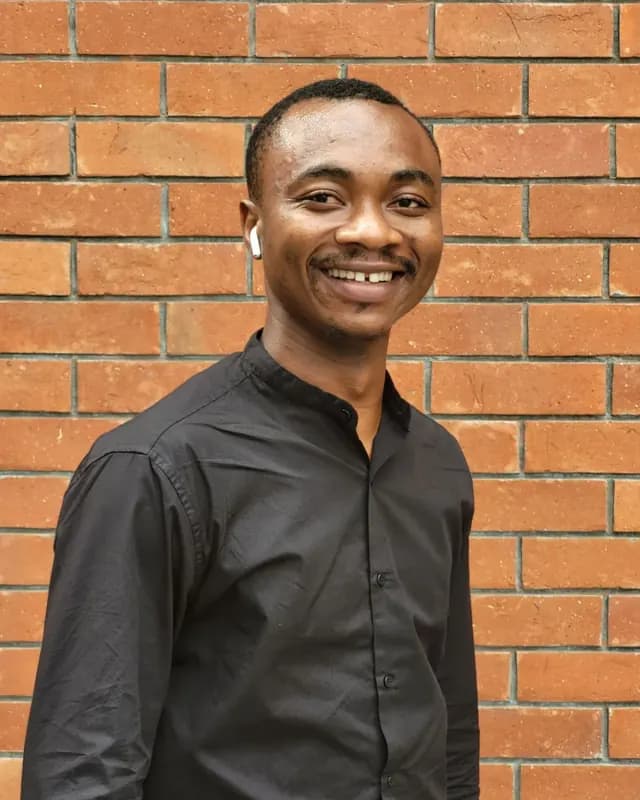 Smiling man in a black shirt in front of a brick wall